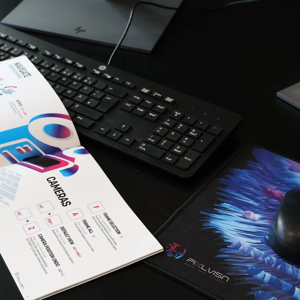Close-up of a workspace featuring an HP keyboard, PIXL VISN mousepad, mouse, and an open booklet displaying colorful camera navigation tips.